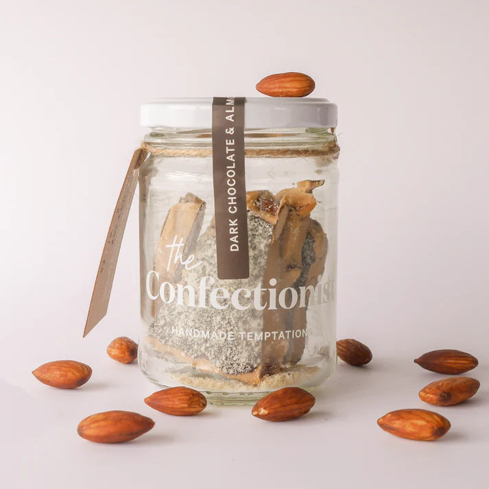 Glass jar with dark chocolate and almonds on a light background