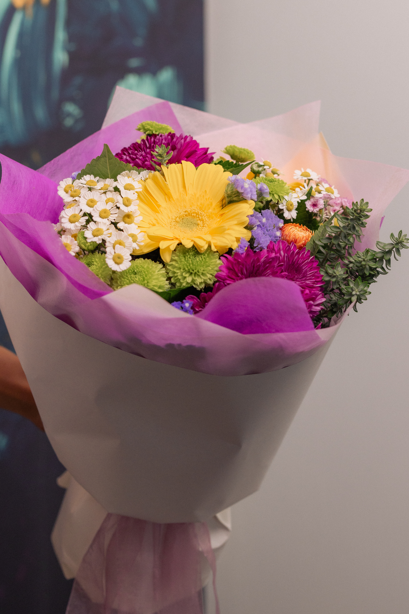 Bouquet of bright seasonal fresh flowers wrapped in purple paper with a blurred background